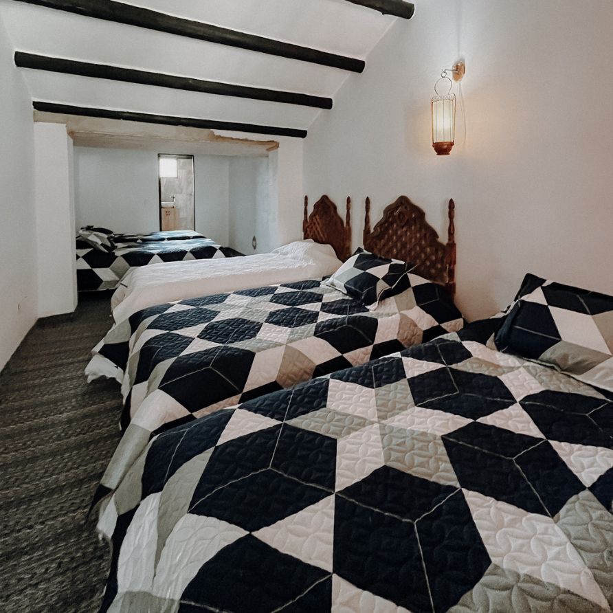 Habitación rústica con cama de madera y ventanas coloniales en una hacienda.