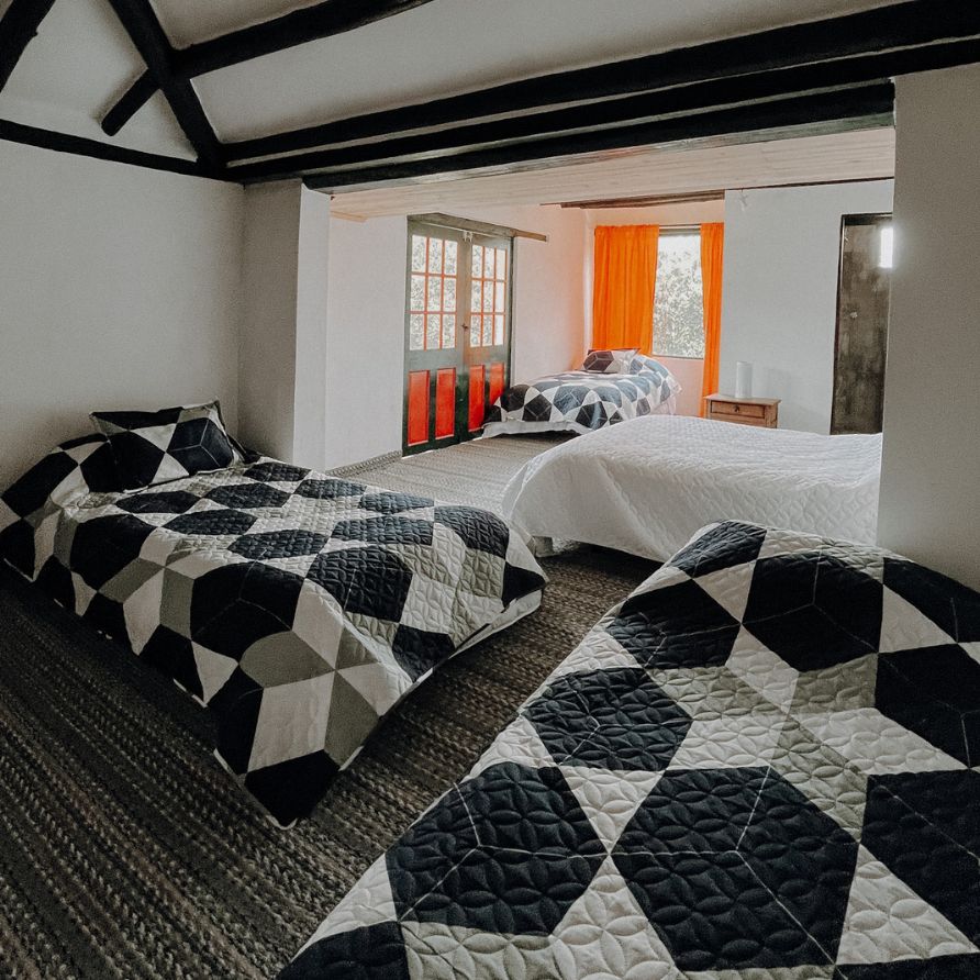 Habitación rústica con cama de madera y ventanas coloniales en una hacienda.