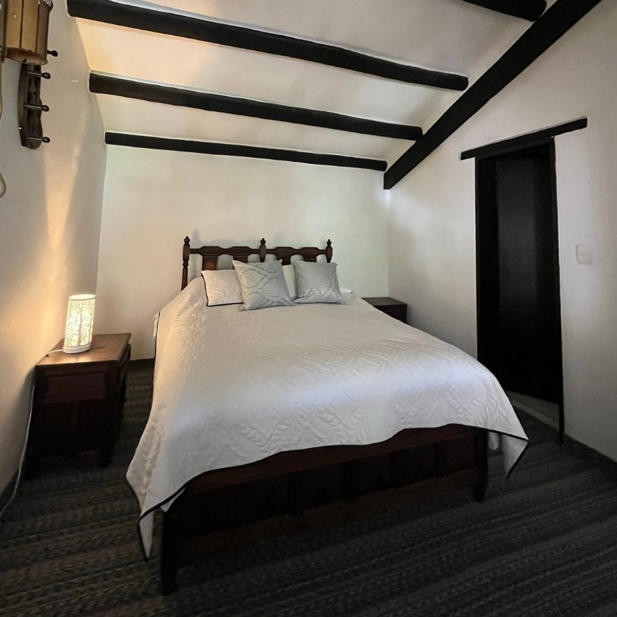 Habitación rústica con cama de madera y ventanas coloniales en una hacienda.