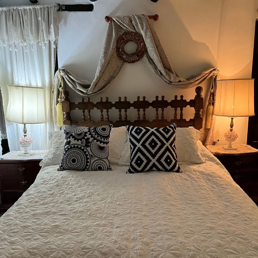 Habitación rústica con cama de madera y ventanas coloniales en una hacienda.